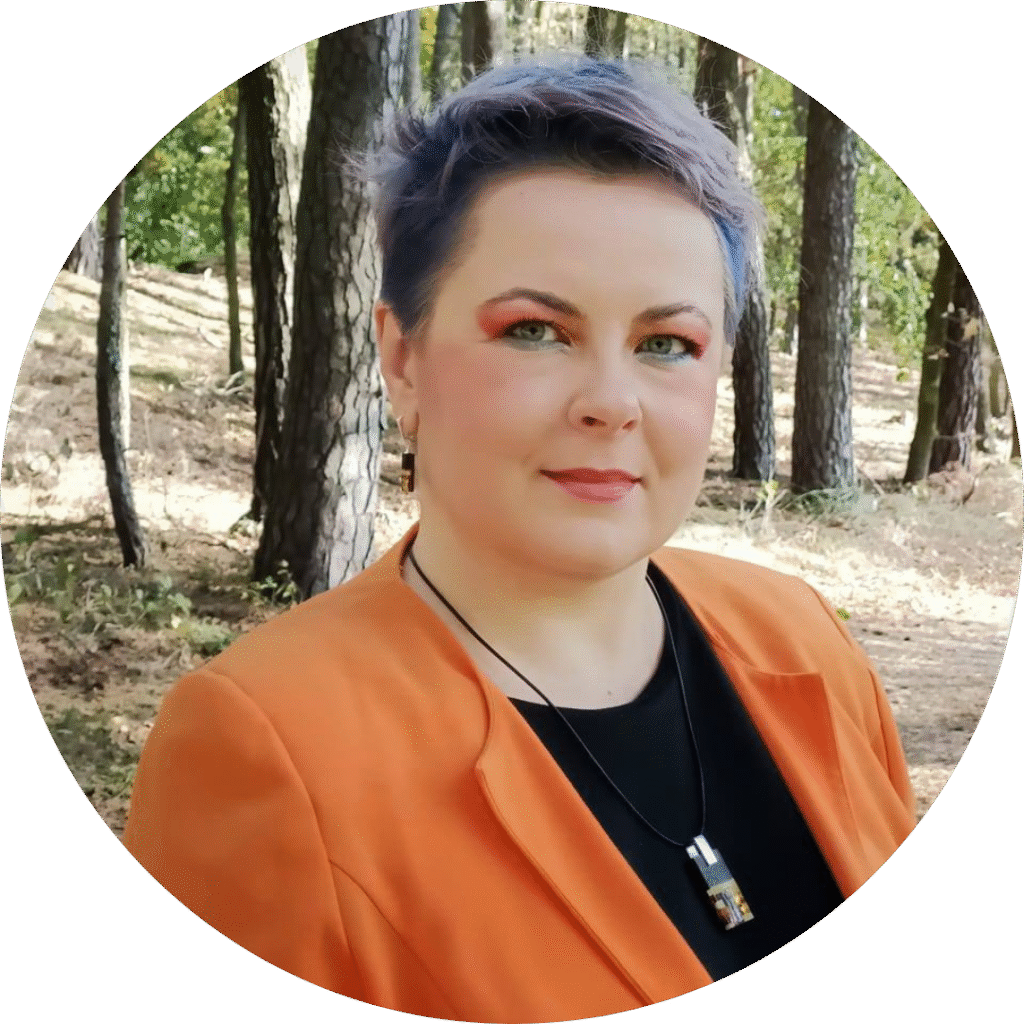 Portret Darii - uśmiechniętej kobiety z krótkimi, niebiesko-fioletowymi włosami, ubranej w czarną koszulkę pod pomarańczową marynarką.